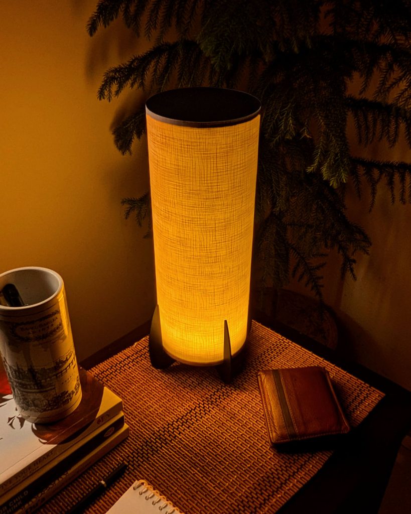 A cylindrical shaped japandi style jute fabric lamp on a sidetable set in a warm cozy tone.